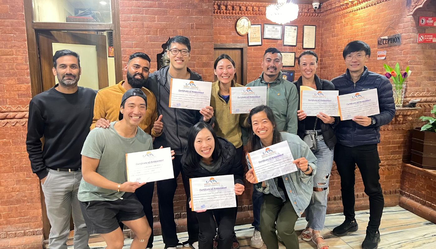 Group of happy trekkers holding ‘Certificate of Achievement’ from Nepal Hiking Adventure after completing the Annapurna Circuit Trek, inside a hotel in Kathmandu.