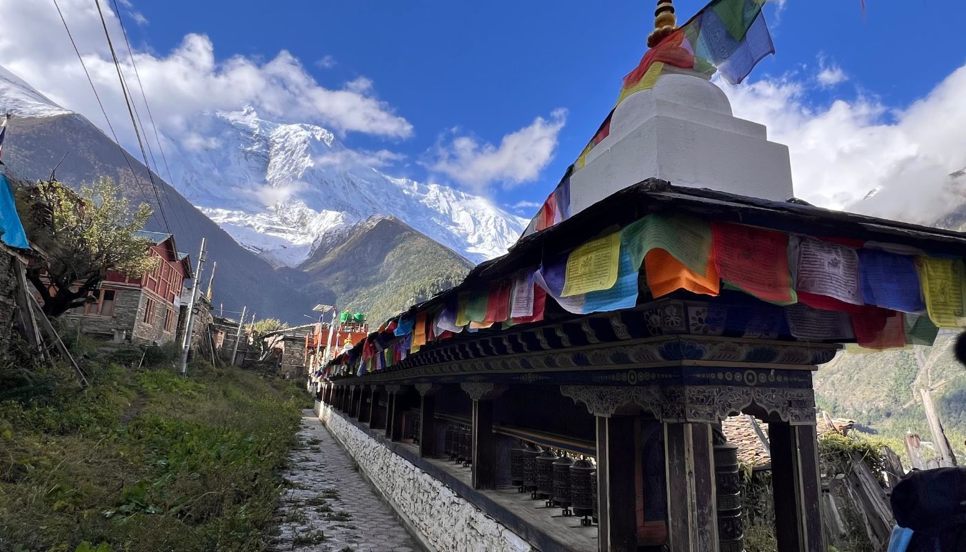 Scenic view of Manang Village with colorful prayer flags and mani wall, surrounded by snow-capped Annapurna peaks along the Annapurna Circuit Trek .