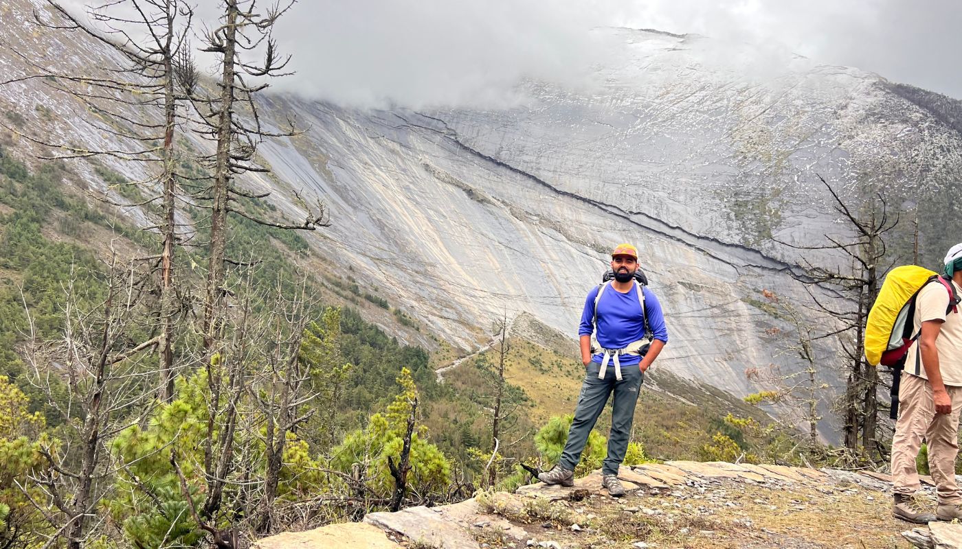 Trekker standing in front of the massive curved Paungda Danda rock face between Chame and Pisang on the Annapurna Circuit Trek.