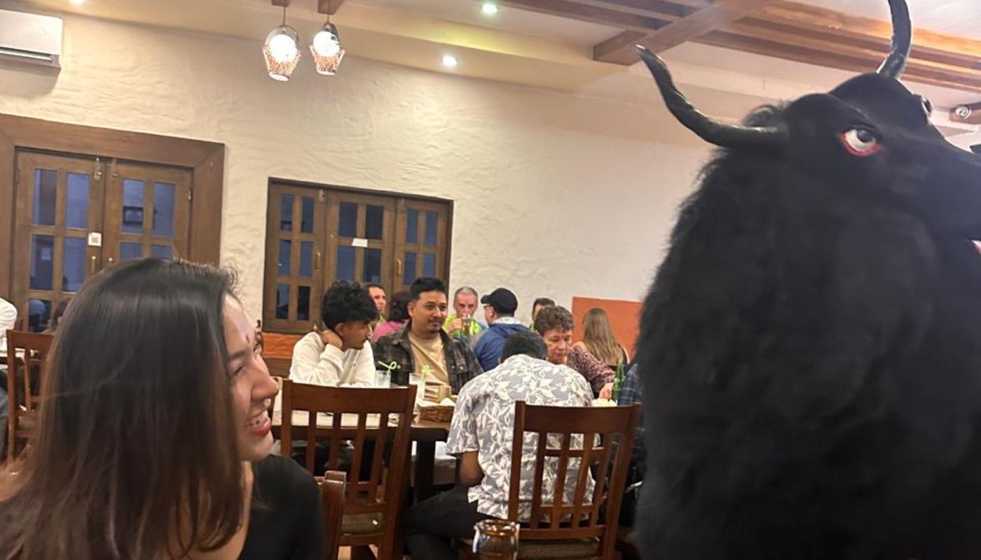 Trekkers enjoying a warm meal during the Annapurna Circuit Short Trek, with a playful yak mascot illustration nearby.